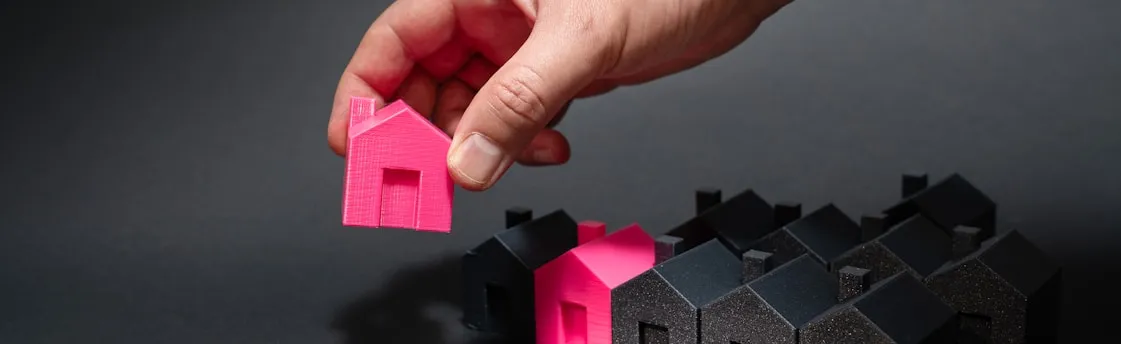 A hand reaching for a pink house in front of a row of houses