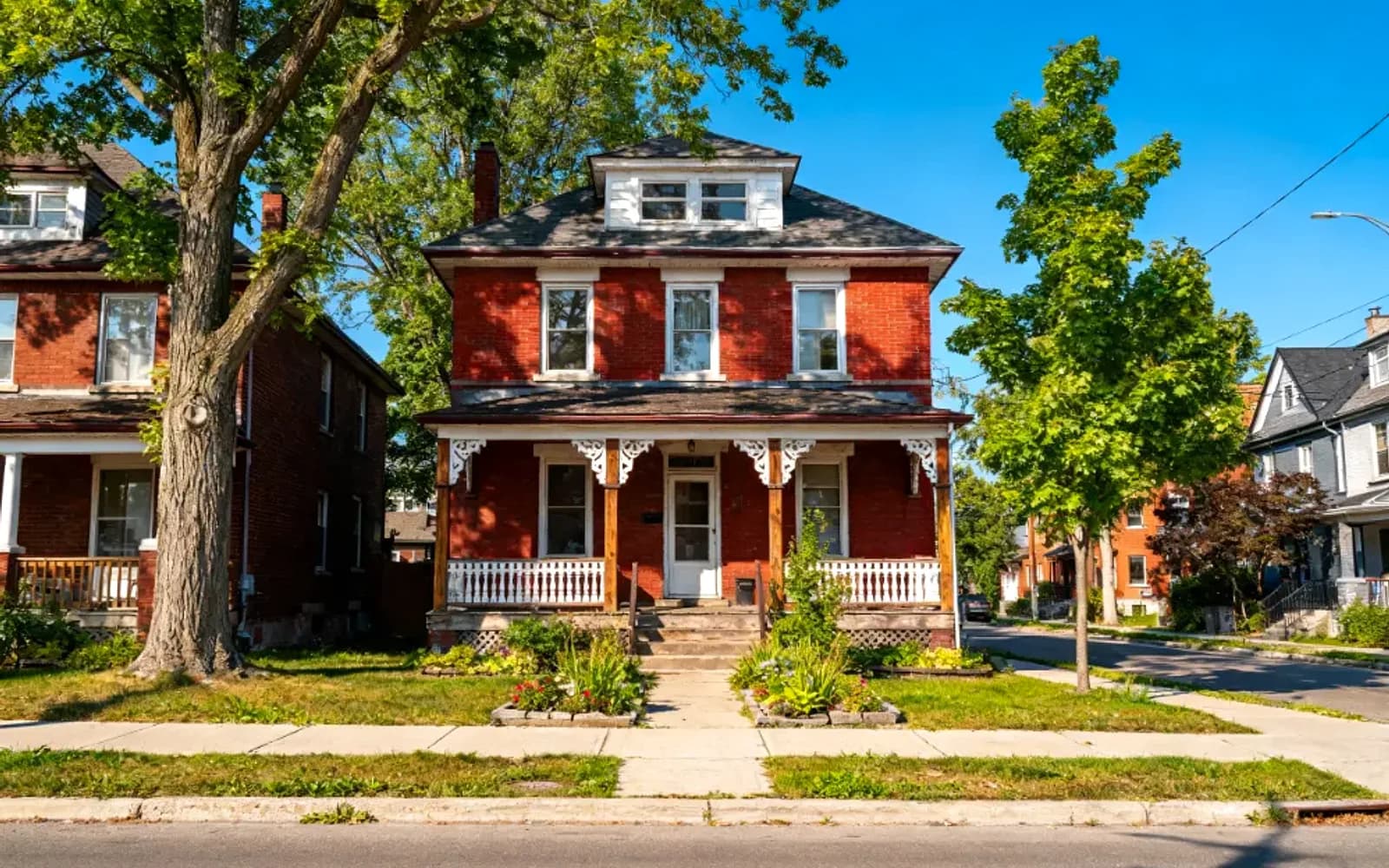 Red-brick two-storey century home with a covered porch on a tree-lined street in Bridgenorth, Ontario