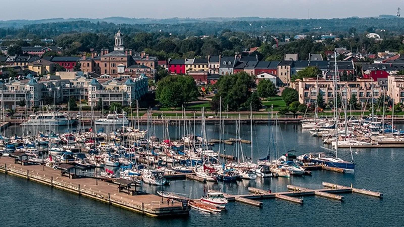 Aerial view of Cobourg's harbour and marina full of sailboats, with the waterfront town and Victoria Hall's cupola beyond