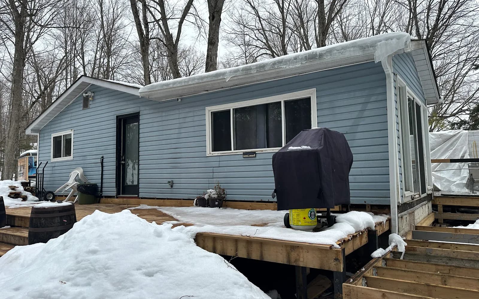 Pale blue single-storey home with a wood deck on a wooded winter lot in King City, Ontario