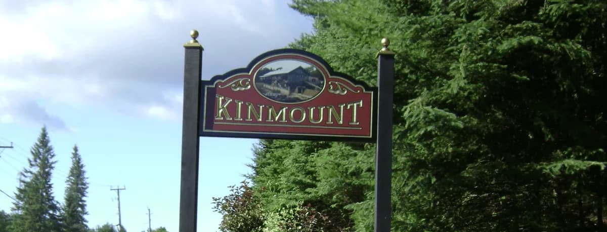 The wooden Kinmount village welcome sign framed by evergreen trees