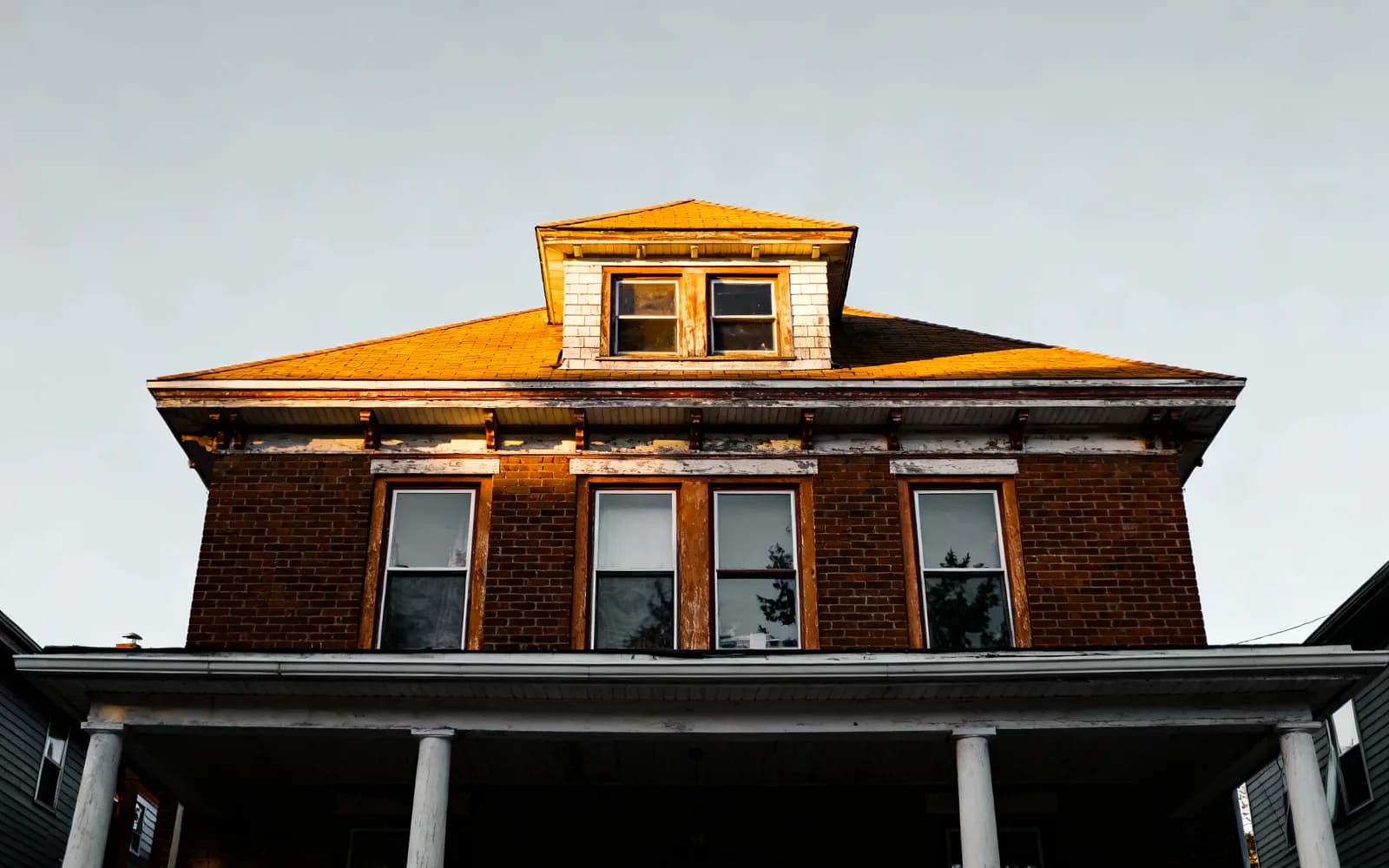 Older two-and-a-half-storey brick home with a dormer and covered porch at golden hour in Kitchener-Waterloo, Ontario