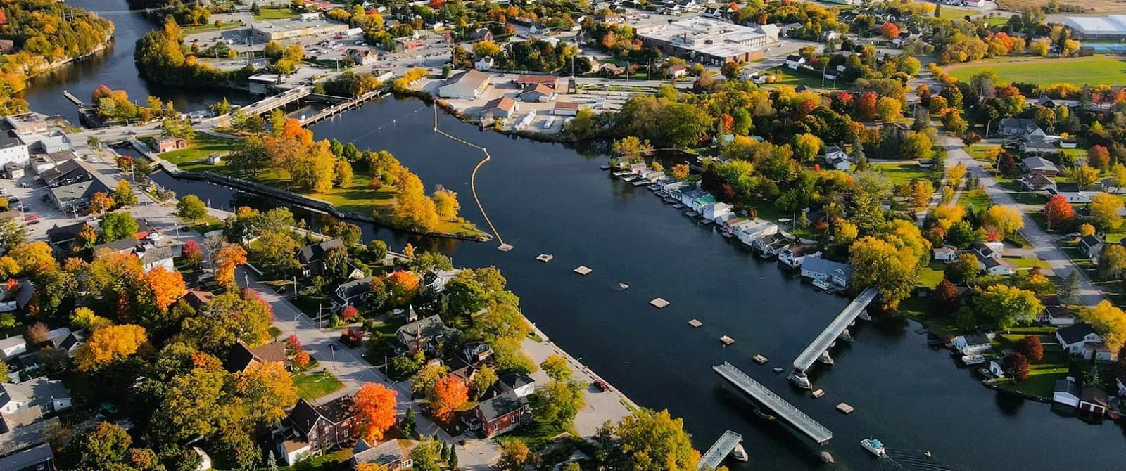 Aerial view of a Kawartha lock town along a channel lined with boathouses and autumn trees