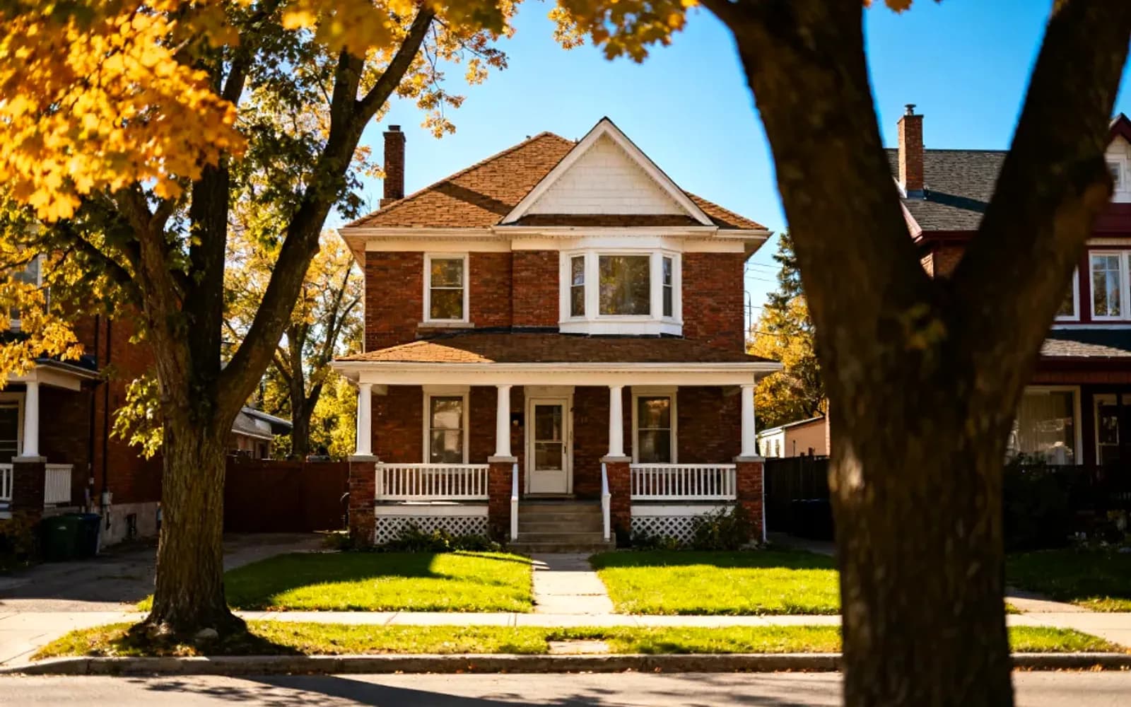Brick two-and-a-half-storey home framed by autumn trees in Ajax, Ontario