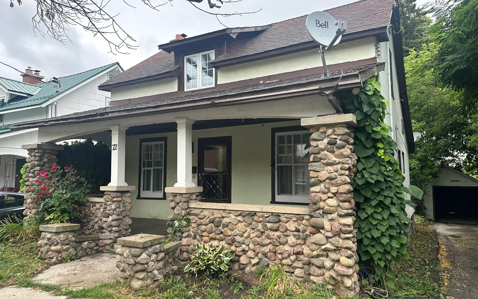 Character stucco home with a stone-pillar covered porch on a leafy street in Bolton, Ontario