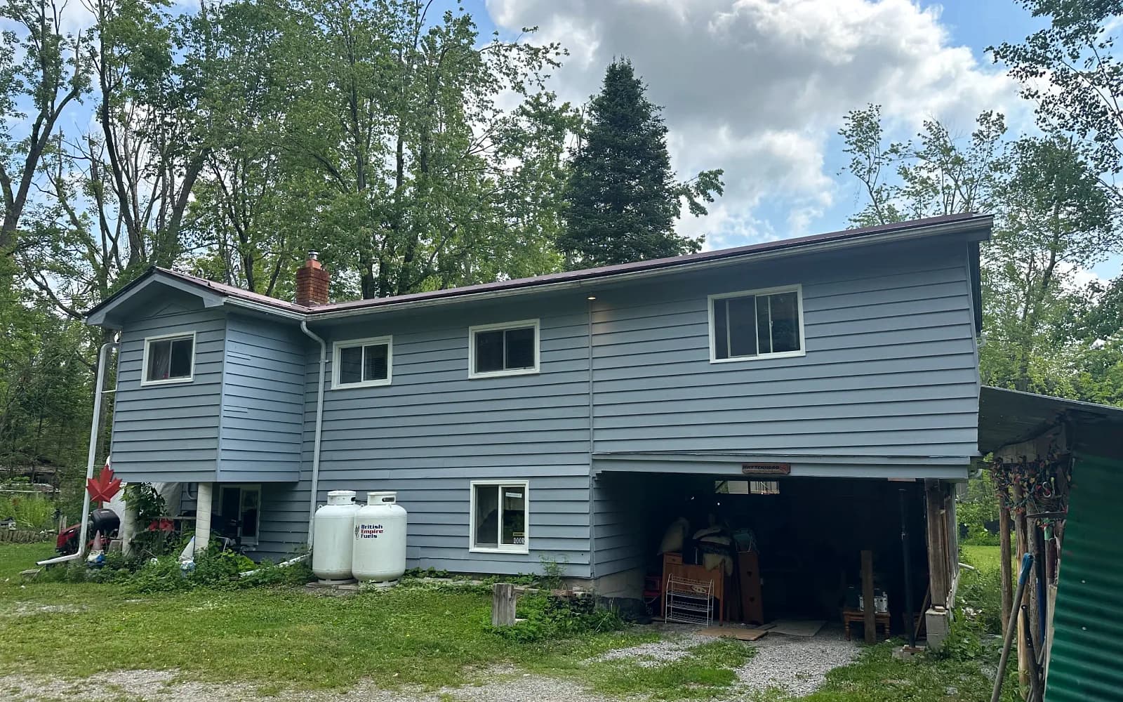 Blue-sided raised home on a wooded lot with a gravel drive in Bowmanville, Ontario