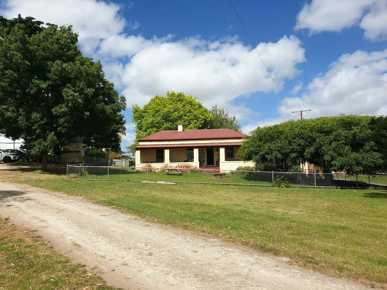 Country home with a metal roof and mature trees behind a fence along a gravel lane in rural Mono