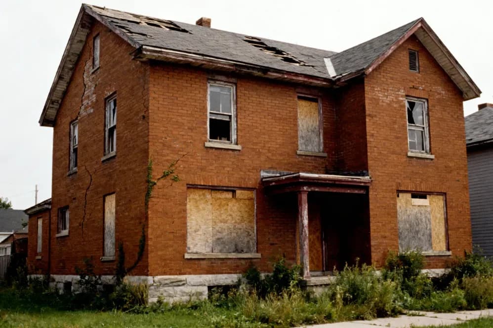 Boarded-up red-brick two-storey farmhouse with a damaged roof being sold as-is in Norfolk County, Ontario