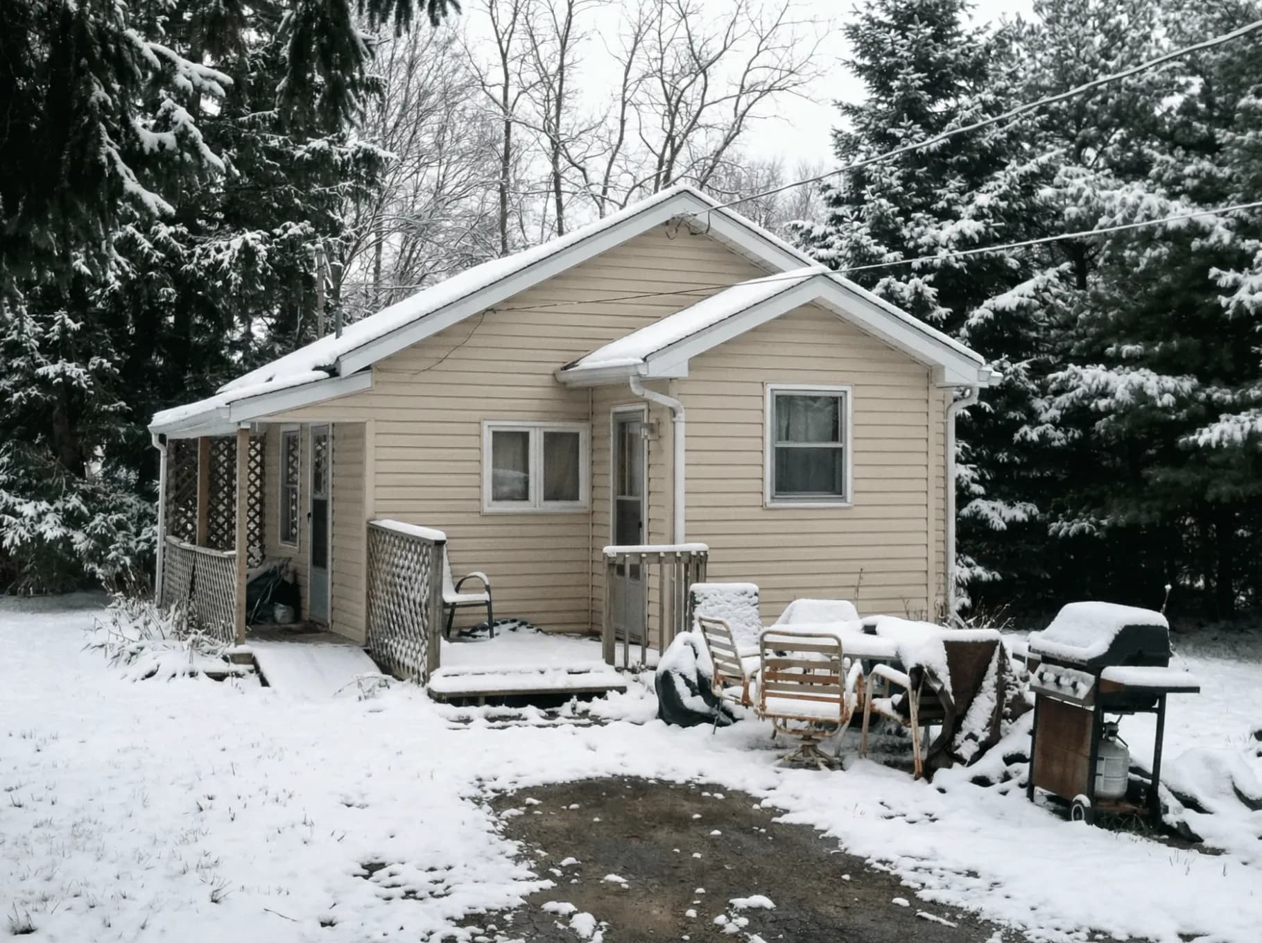 Beige bungalow with a covered porch in a snowy wooded yard in Caledon, Ontario