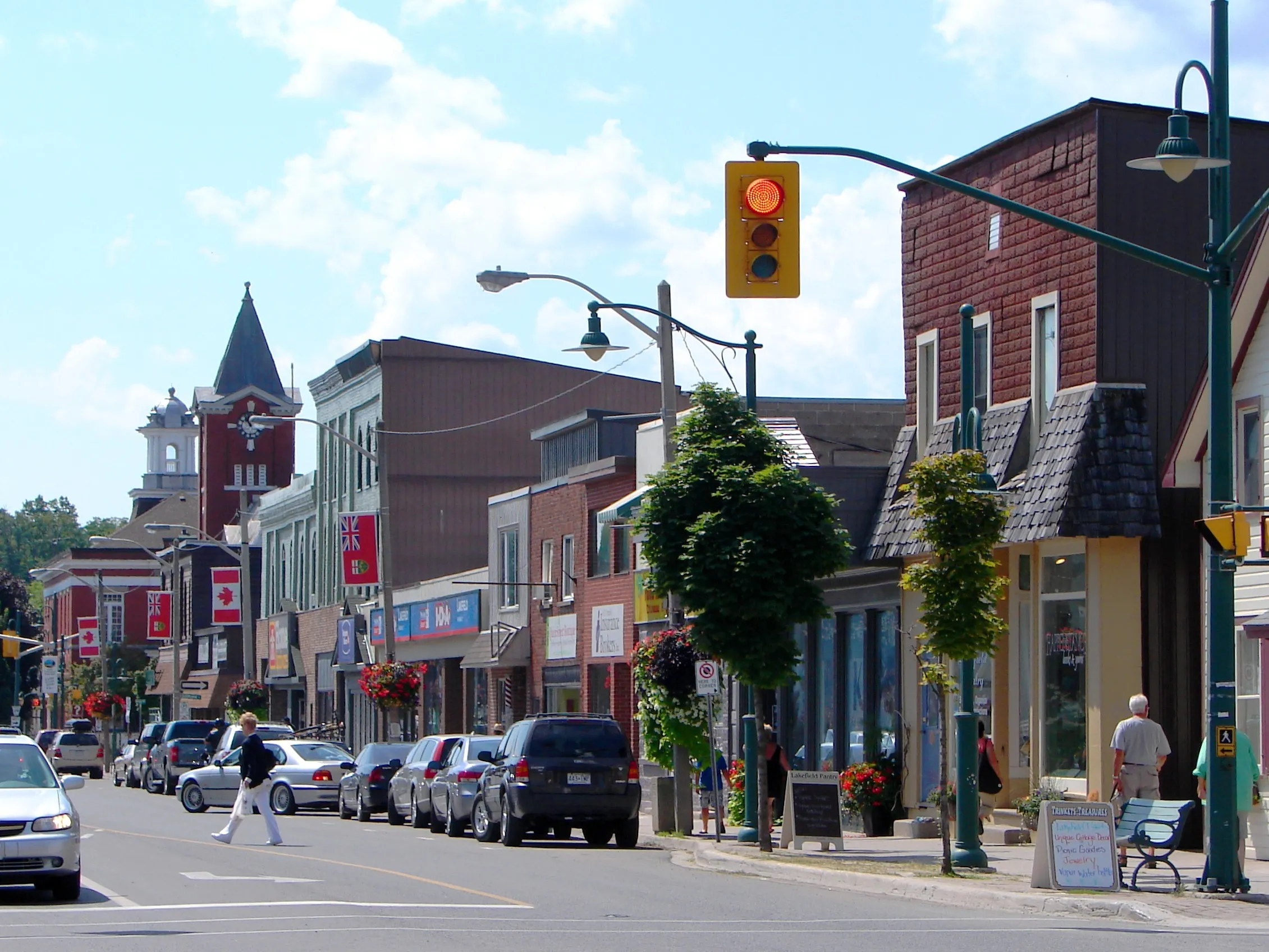 Downtown Lakefield main street in the Township of Selwyn, with a historic brick clock tower, storefronts and Canadian flags on a sunny summer day