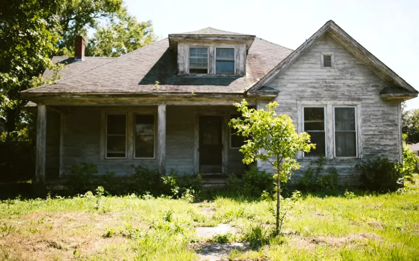 Weathered white farmhouse with an overgrown yard, sold as-is near Wasaga Beach, Ontario