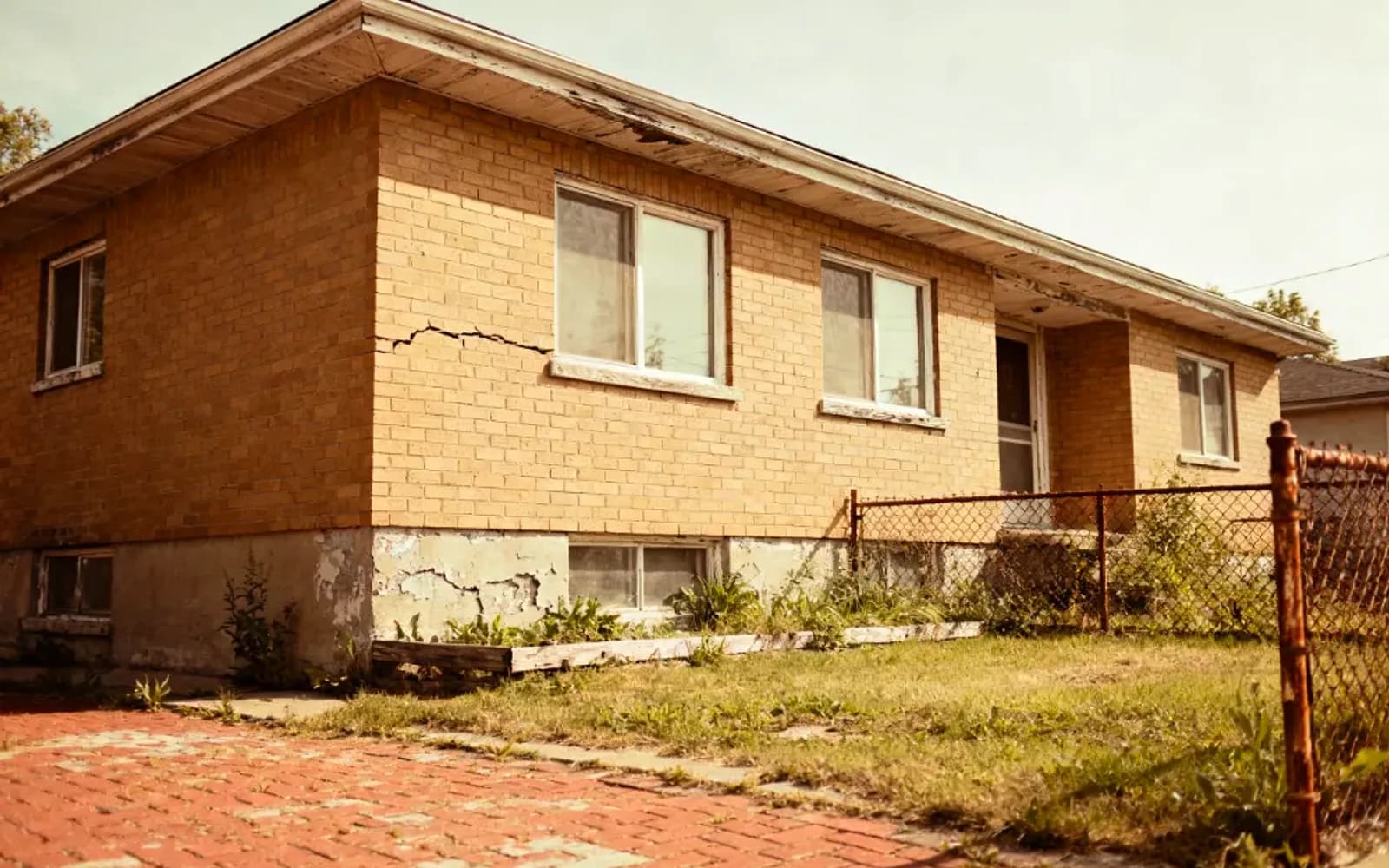 Yellow-brick bungalow with a cracked foundation and chain-link fence in Welland, Ontario